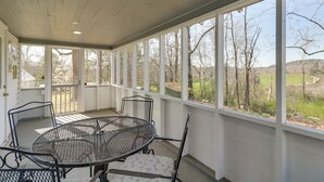 Une terrasse couverte avec une table ronde et des chaises, de grandes fenêtres et une vue sur les arbres et les collines.