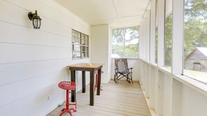Une véranda avec une table et des chaises, une fenêtre et un luminaire fixé au mur.