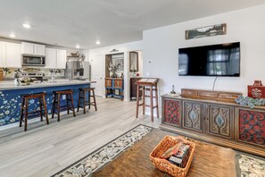 A modern kitchen with white cabinets, a large island with stools, a flat-screen TV, and a decorative cabinet with intricate metalwork. - 6 Mi to Camp Lejeune! Family Home w/ Koi Pond (Jacksonville)