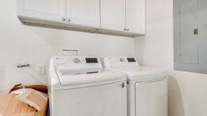 Uma lavanderia com duas máquinas de lavar e secar frontais brancas, um armário branco acima e uma porta à direita.