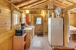A wooden cabin interior with a kitchen, a dining area, and a bedroom.