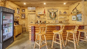 Um espaço de bar rústico com banquetas de madeira, um frigorífico cheio de bebidas e um sinal a indicar a zona de mercearia.
