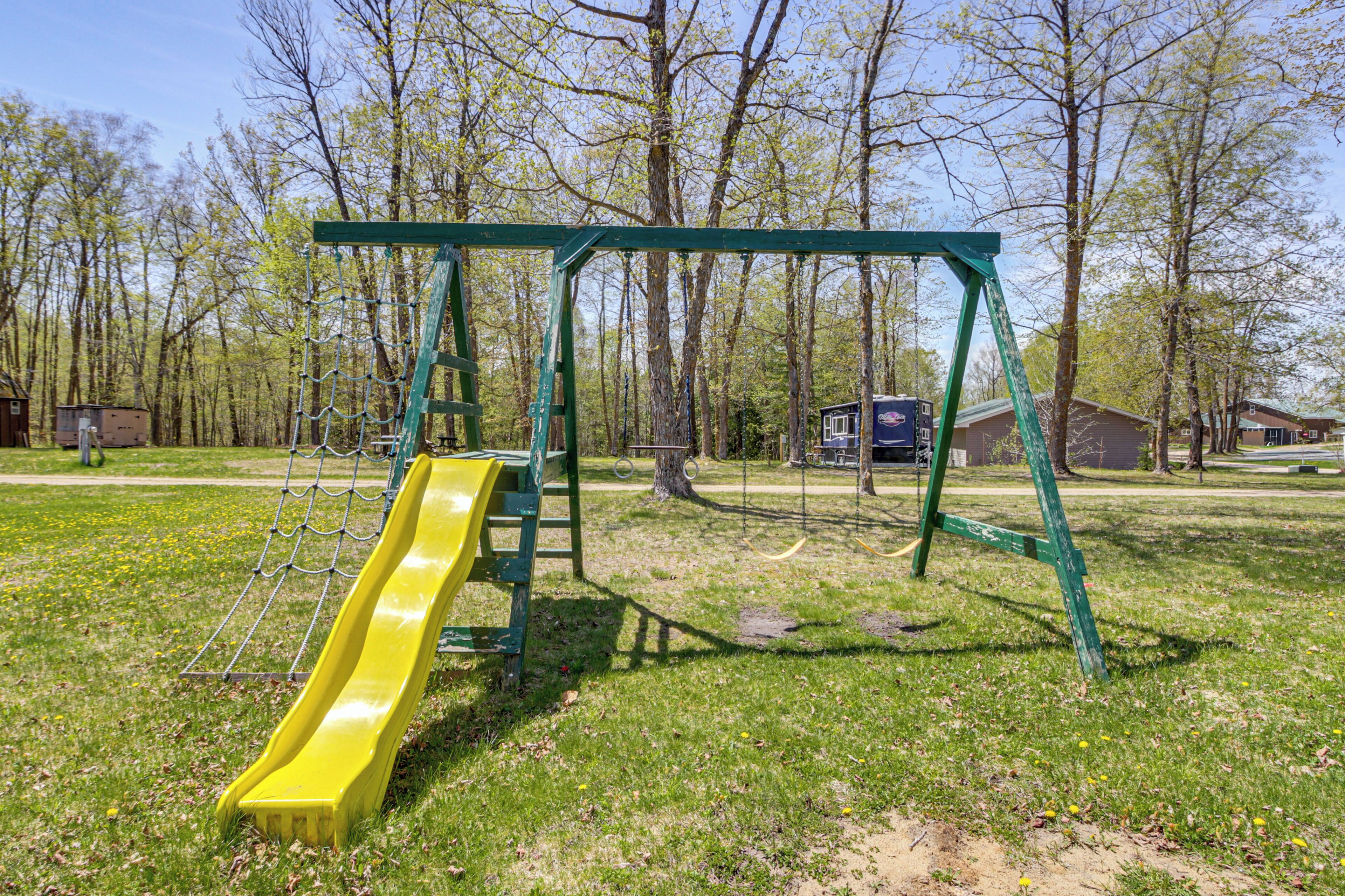 A playground with a yellow slide and swings in a grassy area with trees and houses in the background.
