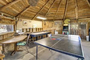A rustic wooden room with a ping pong table, a small table with chairs, and a pegboard wall with various items.