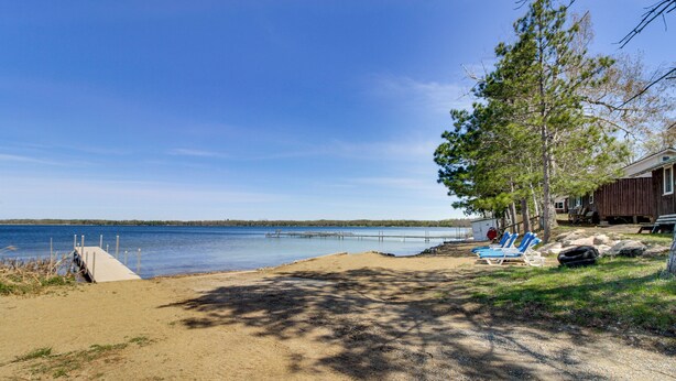 A beach with a wooden dock, a sandy area, and a building with a porch. - Minnesota Lake Escape! Waterside Resort Cabin (Tenstrike)