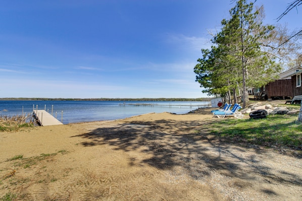 A beach with a wooden dock, a sandy area, and a building with a porch. - Minnesota Lake Escape! Waterside Resort Cabin (Tenstrike)