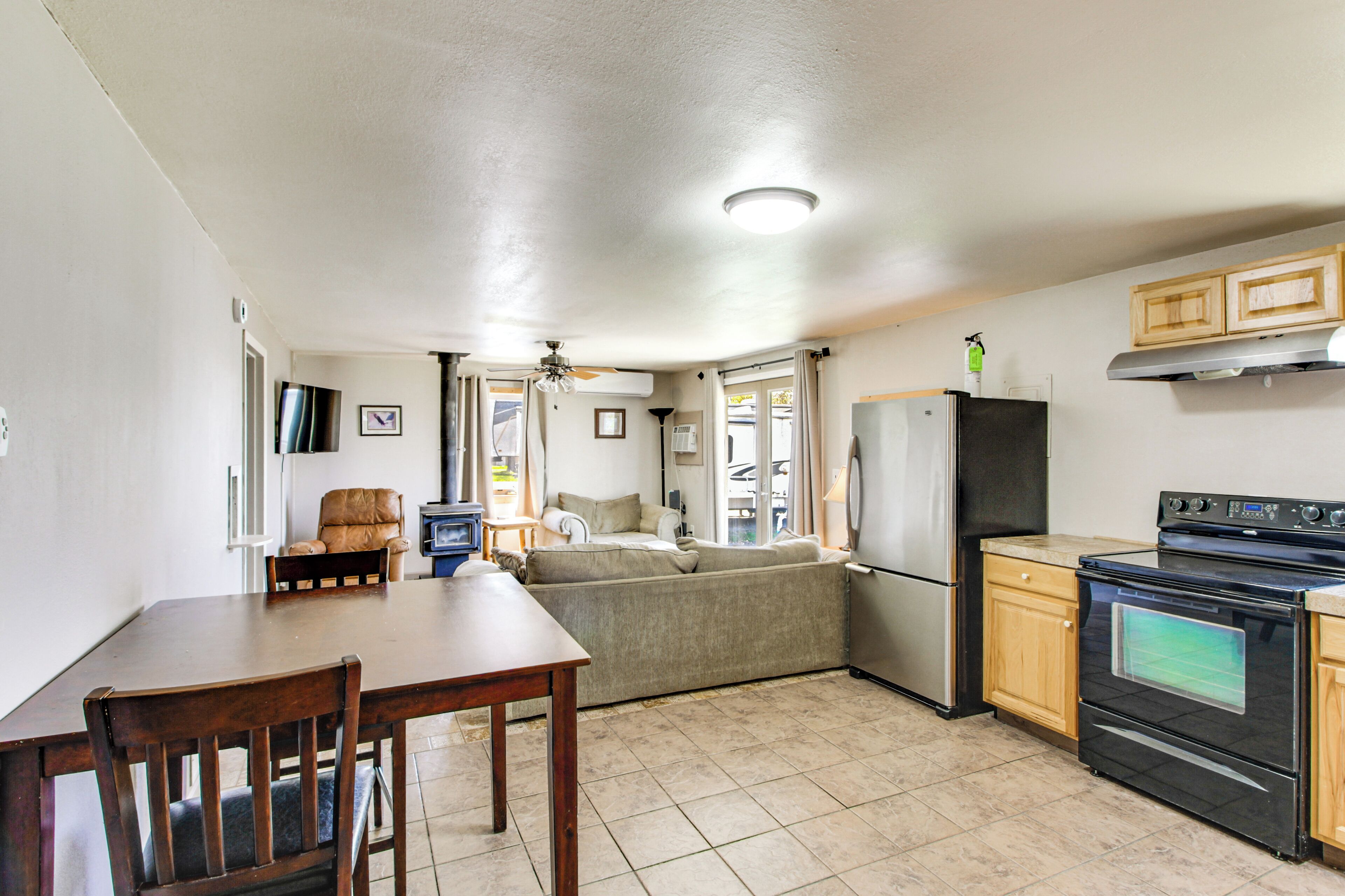 A compact kitchen with a dining table, chairs, a sofa, a refrigerator, an oven, and wooden cabinets.