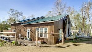 A wooden building with a green roof, a fenced entrance, and a dirt driveway. - Minnesota Lake Escape! Waterside Resort Cabin (Tenstrike)