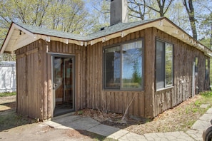 A small wooden cabin with a single door and large windows, surrounded by trees.