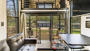 A modern interior with a sofa, a table, and a view of an outdoor deck. - Steps to Gull Lake! Modern RV Stay w/ Resort Perks (Tenstrike)