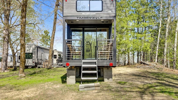 A Timberwolf RV with a ladder leading to a platform, surrounded by trees. - Steps to Gull Lake! Modern RV Stay w/ Resort Perks (Tenstrike)