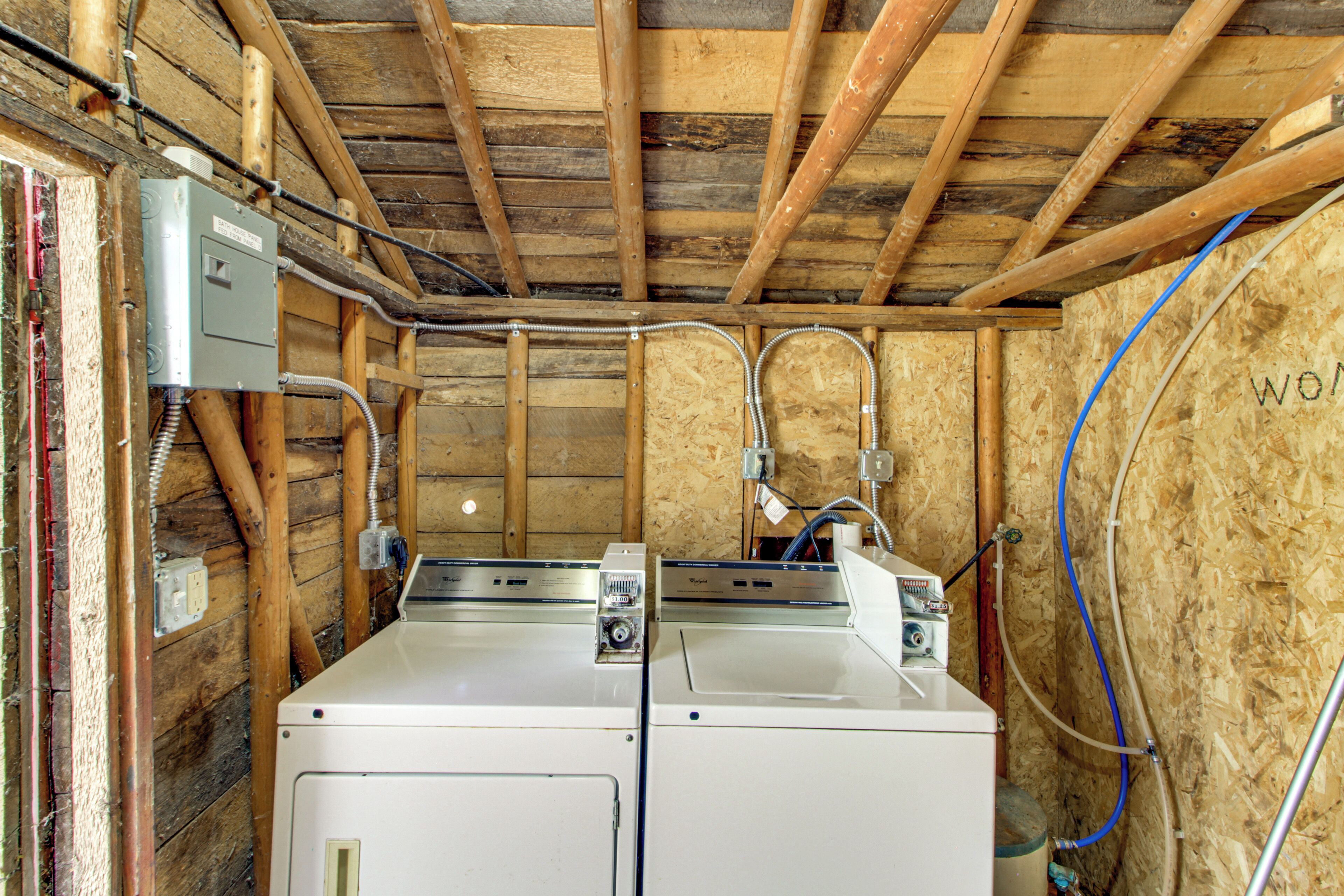 A laundry room with two washers and dryers, wooden walls, exposed ceiling beams, and visible plumbing.