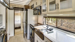 A compact kitchen with a built-in oven, microwave, and a window with a view of trees. - Steps to Gull Lake! Modern RV Stay w/ Resort Perks (Tenstrike)