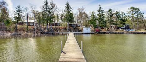 A wooden dock leading to a docked boat, surrounded by trees and a building with a dock.