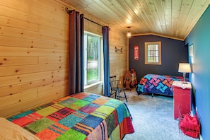 A cabin with two beds, a wooden ceiling, and a window.