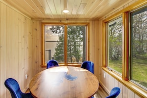 A wooden-paneled room with a round table and blue chairs, large windows with a view of trees and a building outside.