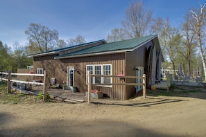 A wooden building with a green roof, a fenced area with chairs, and a dirt path.
