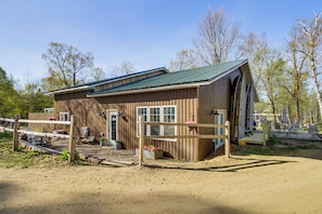 A wooden building with a green roof, a fenced area, and a dirt ground.