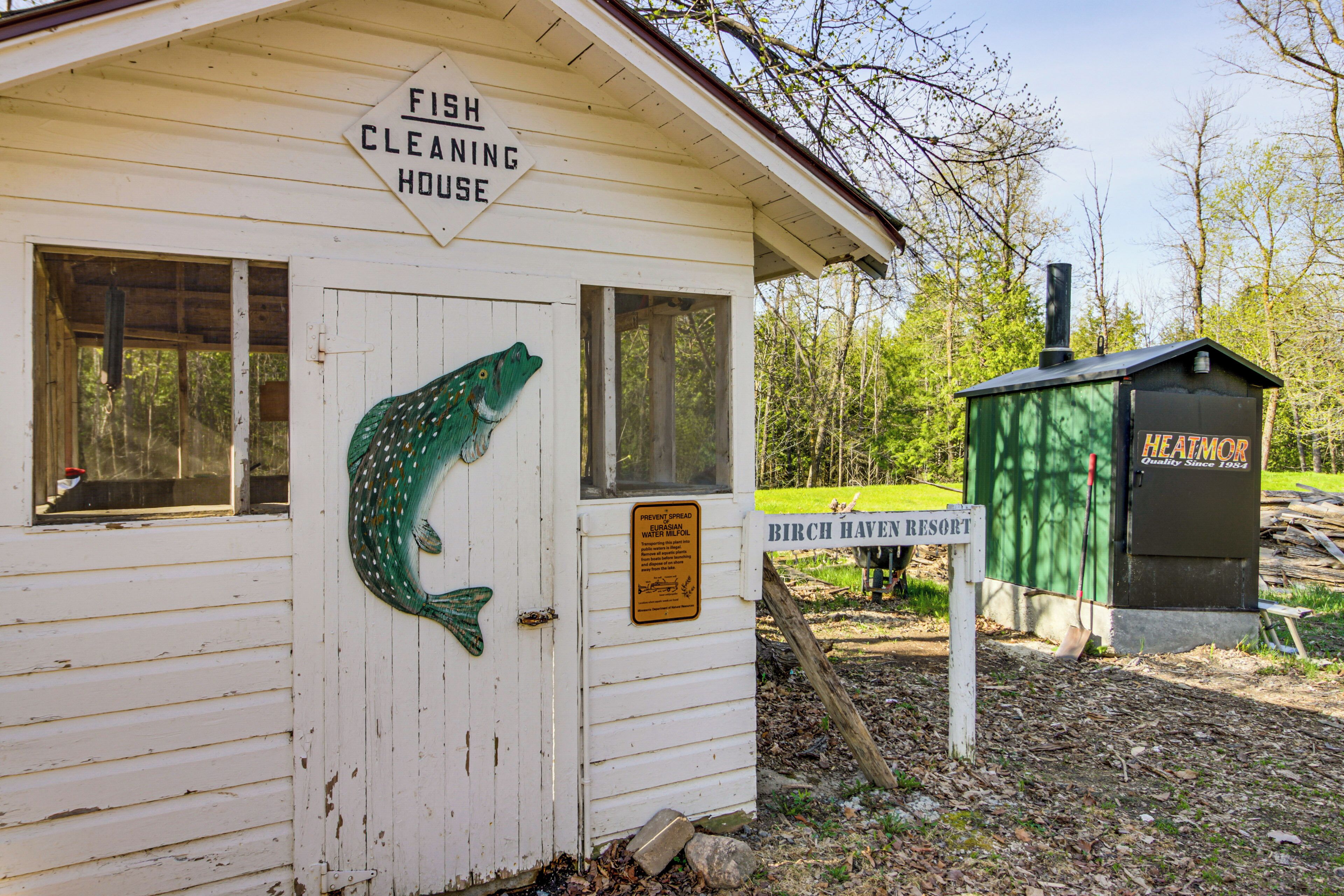 Un abri rustique pour nettoyer le poisson, agrémenté d’une décoration sur le thème du poisson, d’une enseigne indiquant le nom du complexe hôtelier « Birch Haven Resort » et d’un appareil de chauffage vert.