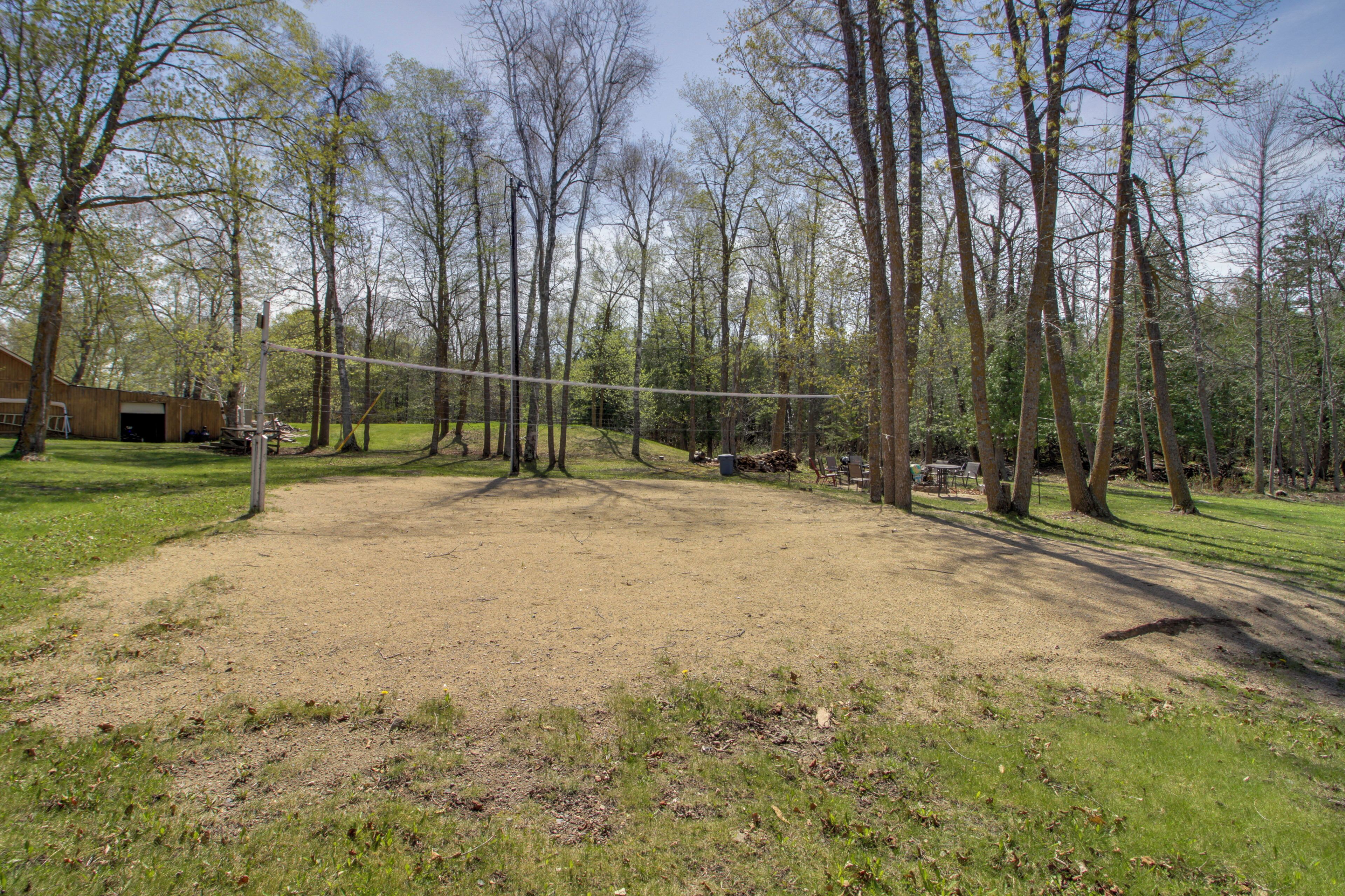 A fenced yard with trees, a volleyball net, and a building in the background.