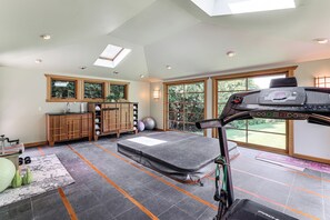 A spacious room with a ceiling fan, exercise equipment, a large window, and a yoga mat.