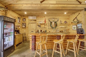 A rustic log cabin interior with a bar area, stools, a refrigerator, and a grocery sign. - For Anglers & Boaters! Beachfront Gull Lake Cabin (Tenstrike)