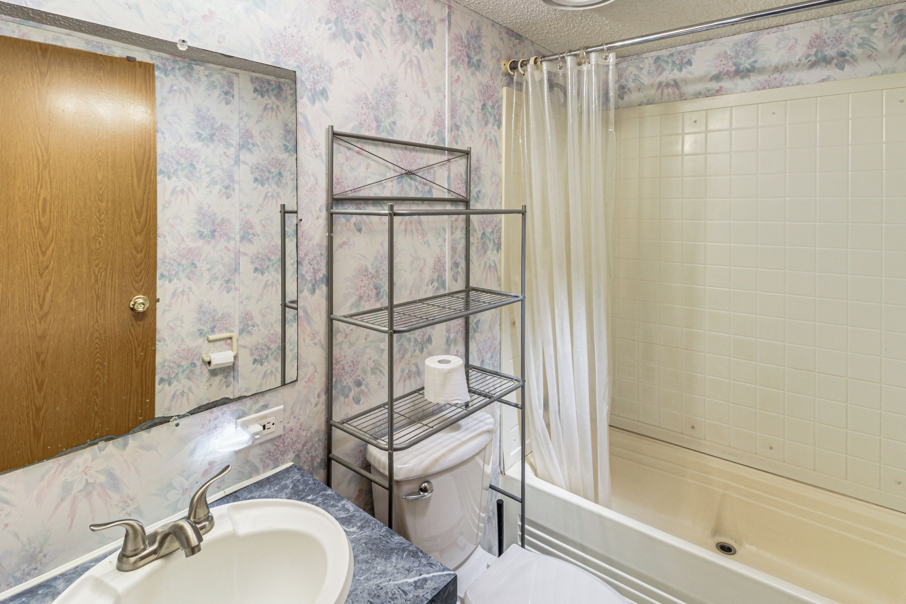 A bathroom with a wooden door, a marble sink, a toilet with a metal shelf, and a shower with a curtain.