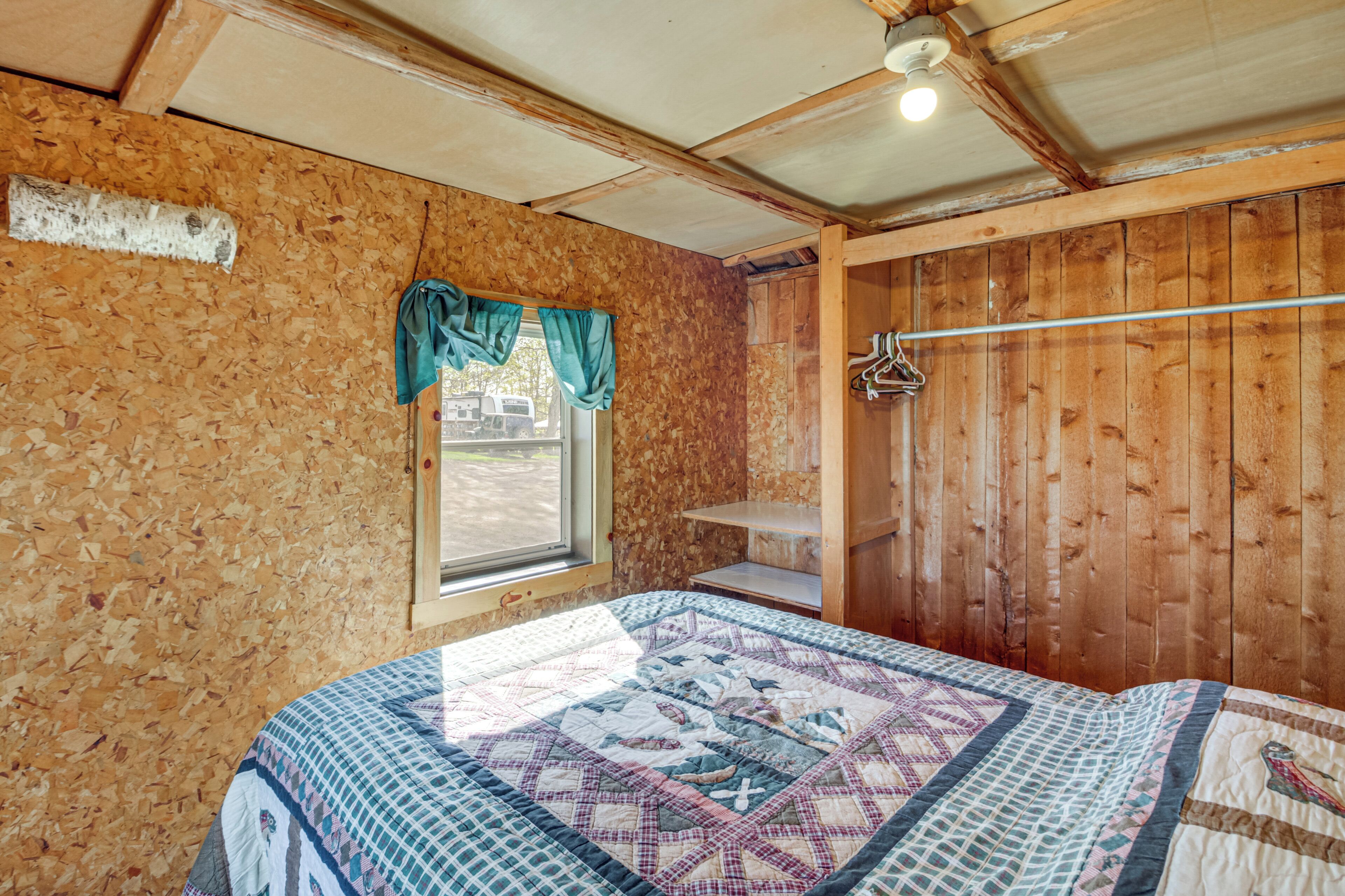 Una habitación con detalles de madera, una cama con colcha, una ventana con cortinas y una puerta con perchero.
