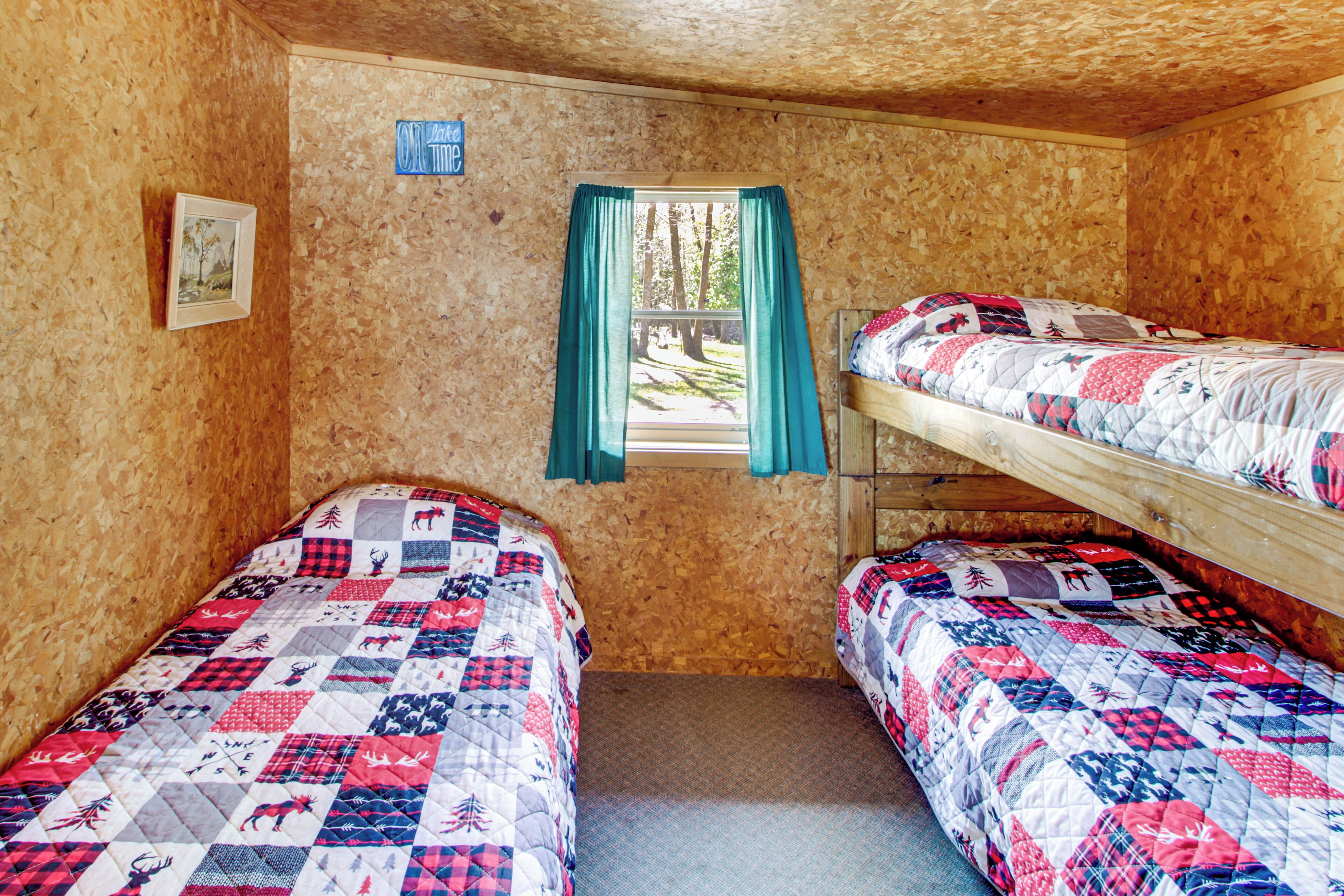 A small, cozy room with two bunk beds, a window with curtains, and a framed picture on the wall.