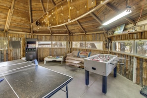 A room with a ping pong table, foosball table, sofa, and windows with views.