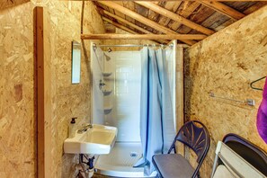 Un baño pequeño y cerrado con ducha, lavamanos y una silla.