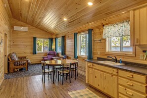 A wooden cabin interior with a dining area, kitchen, and a sofa.
