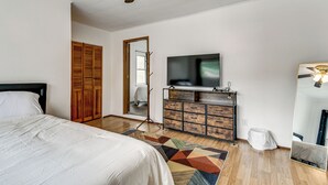 Une chambre à coucher comprenant un lit, une télévision, une commode, un miroir et un ventilateur de plafond.