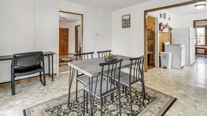 Un espace repas avec une table et des chaises, un tapis, et une cuisine en arrière-plan.