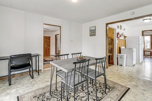A dining area with a table and chairs, a kitchen in the background, and a patterned rug on the floor.
