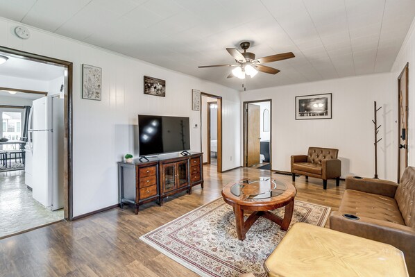A living room with a ceiling fan, a television, a brown leather sofa, a wooden coffee table, and a patterned rug.