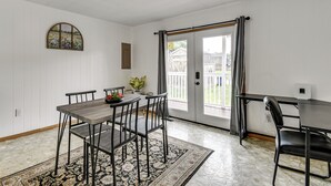 Un coin repas comprenant une table et des chaises, un tapis, un tableau accroché au mur et une vue à travers une porte.