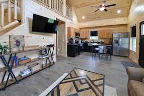 A wooden cabin interior with a TV, kitchen, dining area, and a staircase. - Pet-friendly Home w/ Hot Tub & Yard in Willisburg! (Willisburg)