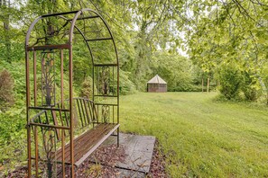 A metal swing set with a bench, surrounded by lush greenery and a small wooden structure in a park. - Walk to Town: Fayetteville Retreat w/ Hot Tub! (Fayetteville)