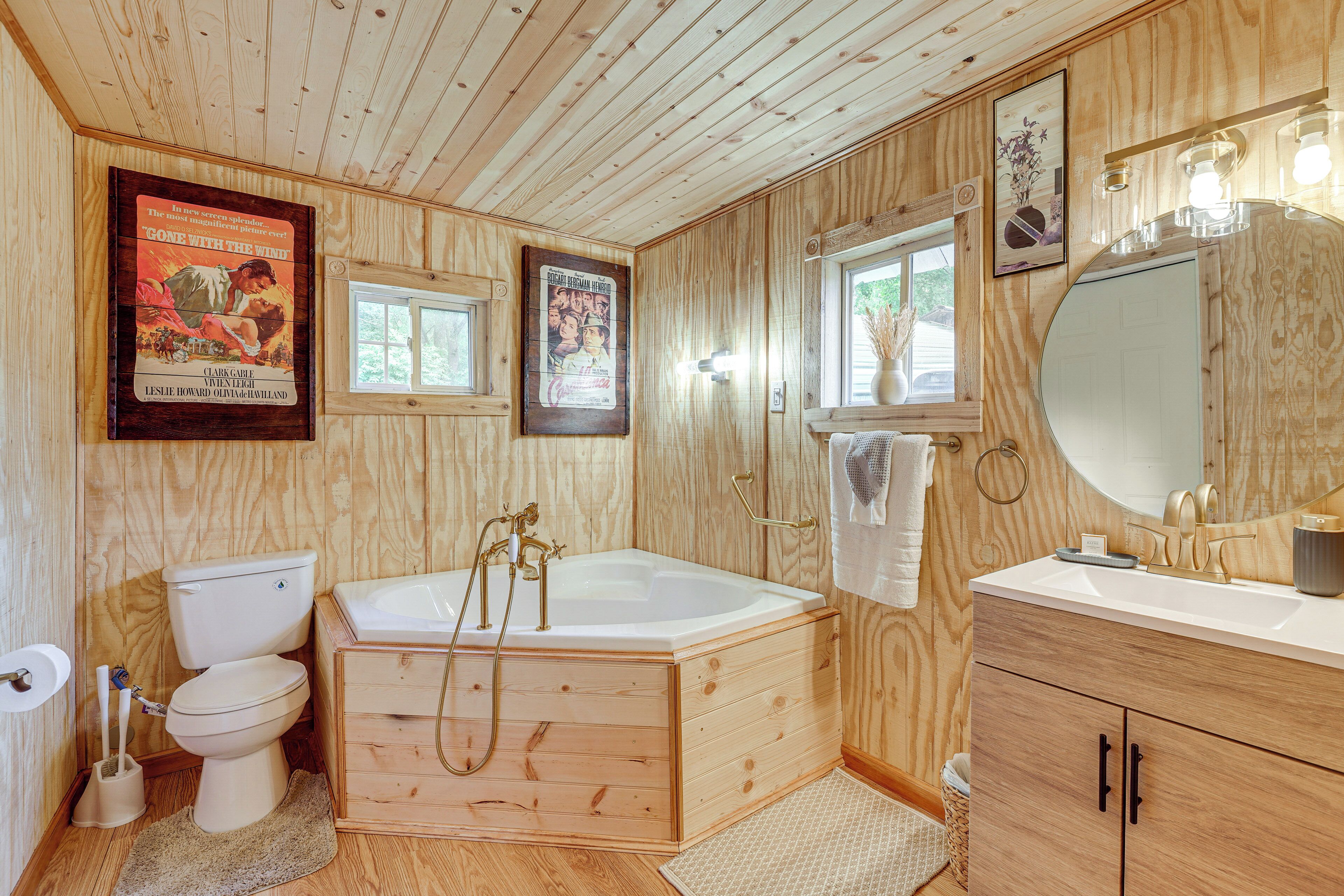 A wooden-paneled bathroom with a toilet, bathtub, vanity, and a large mirror.