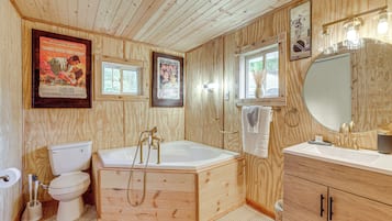 A wooden-paneled bathroom with a toilet, bathtub, vanity, and a large mirror.