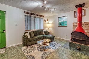 A living room with a green door, a green sofa, a round coffee table, a red chimney, and a window with blinds. - Walk to Town: Fayetteville Retreat w/ Hot Tub! (Fayetteville)