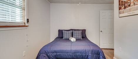 Een slaapkamer met een bed, een plafondventilator, een raam met zonwering, een deur en een schilderij aan de muur.