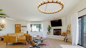Ein Wohnzimmer mit einer Couch, einem Sessel, einem Fernseher, einem Kamin und einem großen Fenster.