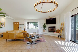 A living room with a sofa, a chair, a TV, a fireplace, and a large window. - Home w/ Outdoor Oasis & Views in Borrego Springs! (Borrego Springs)