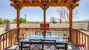 Eine Holzterrasse mit einem Glastisch und Stühlen, mit Blick auf einen Pool und eine Wüstenlandschaft.