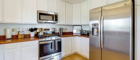 A kitchen with white cabinets, stainless steel appliances, a microwave, stove, oven, and a refrigerator.