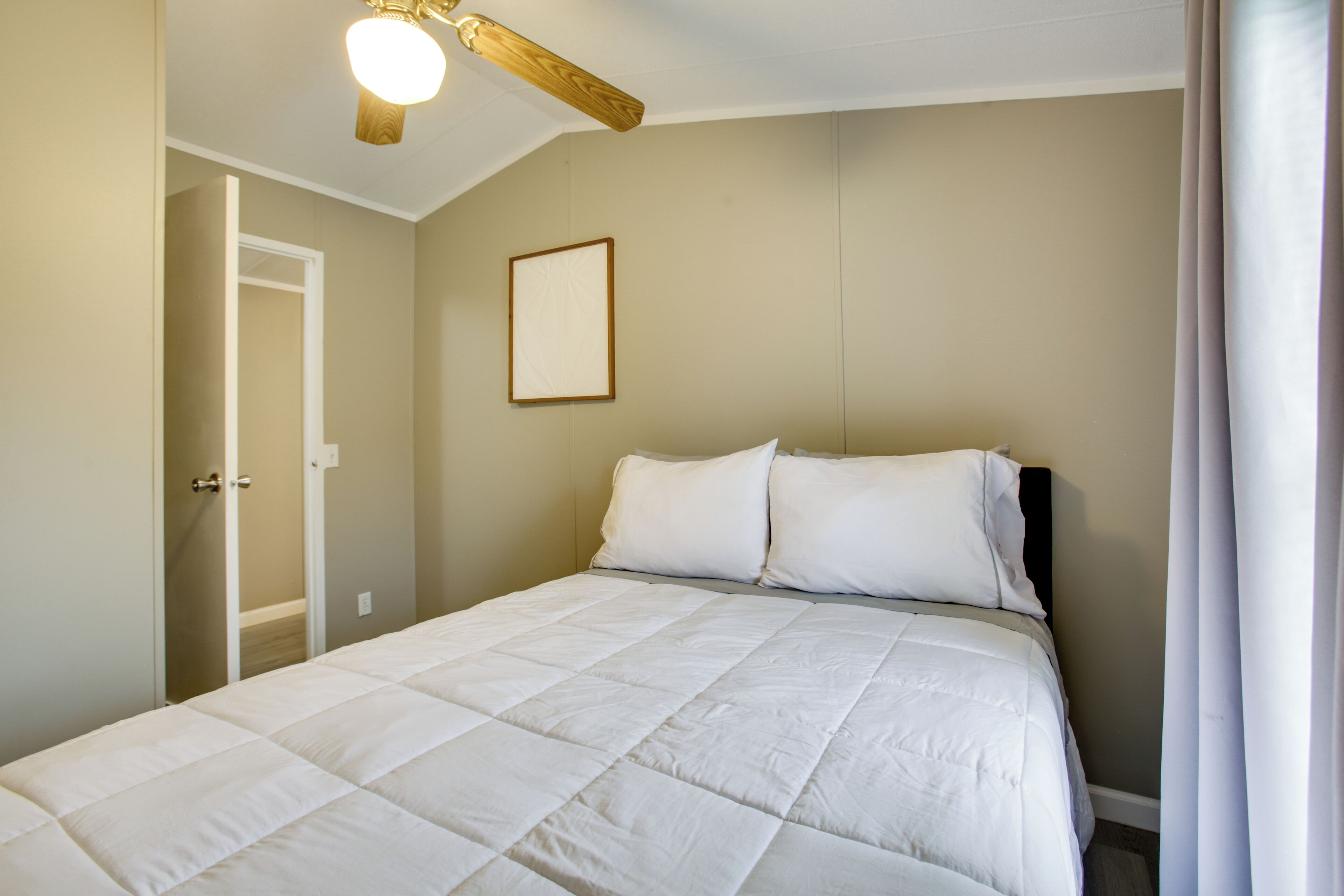 A bedroom with a bed, a door, a ceiling fan, and a framed picture on the wall.