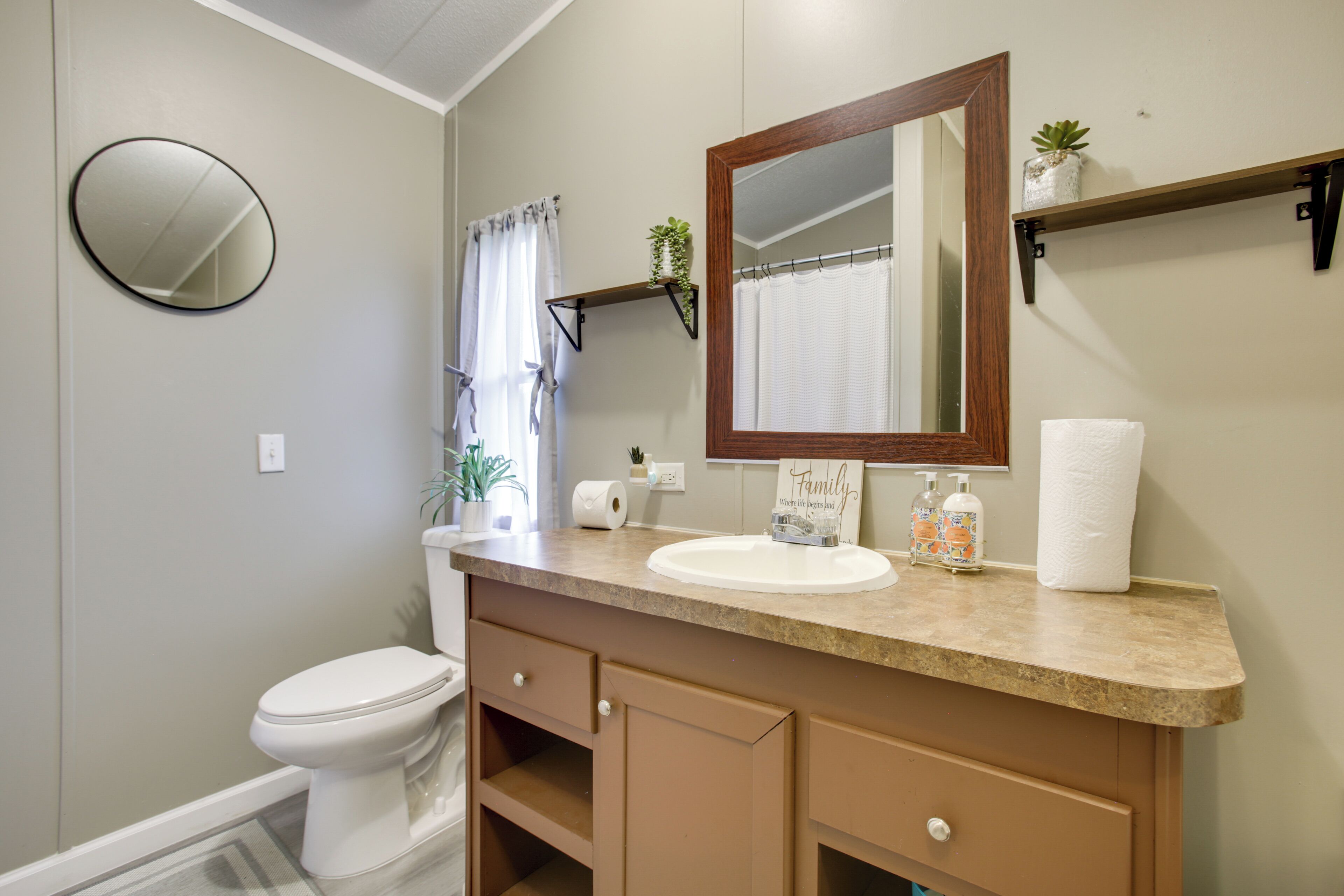 A bathroom with a toilet, sink, mirror, towel rack, and a small shelf with a plant.