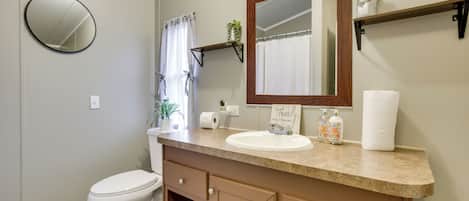 A bathroom with a toilet, sink, mirror, towel rack, and a small shelf with a plant.